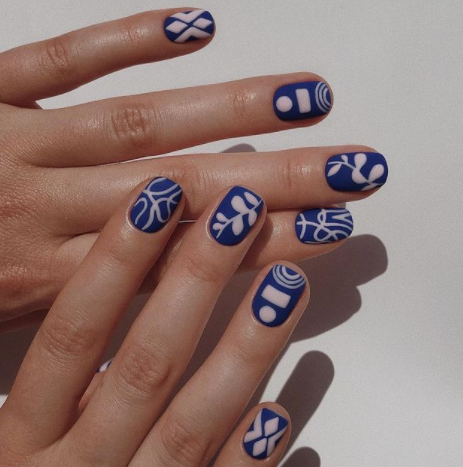 Mãos brancas sobrepostas com unha curta azul com desenhos em branco fosco