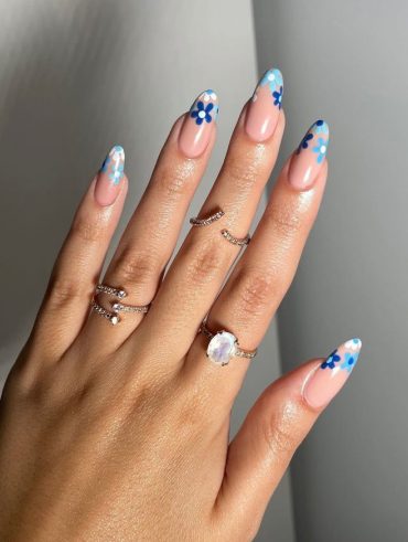 Mão branca com anéis e unha com flores azuis na ponta