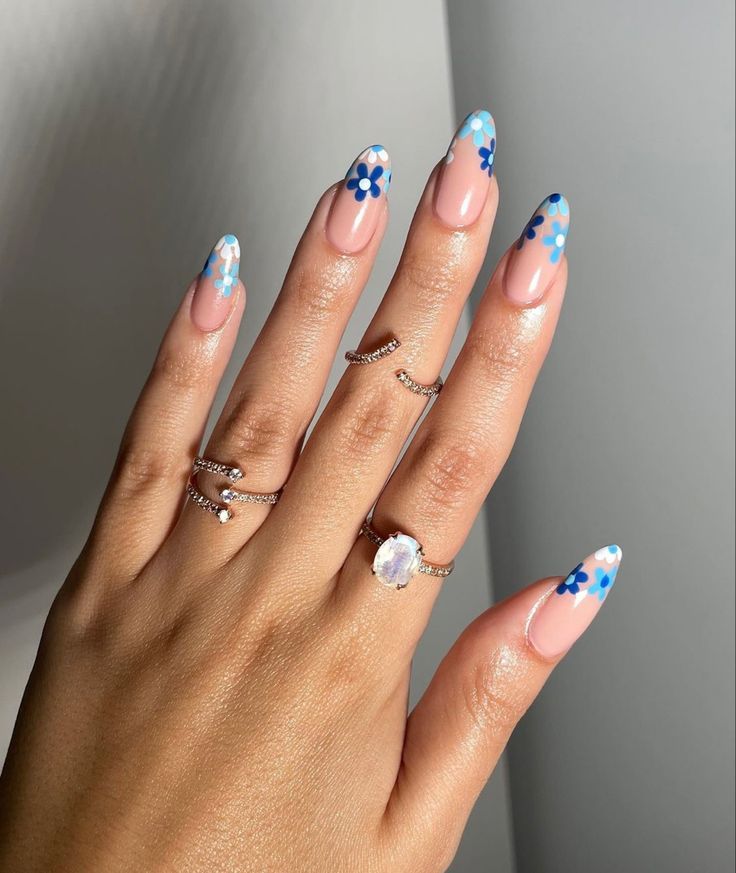 Mão branca com anéis e unha com flores azuis na ponta