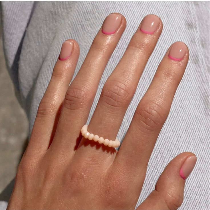 Mão branca com anel de miçanga e unha curta transparente com francesinha rosa invertida