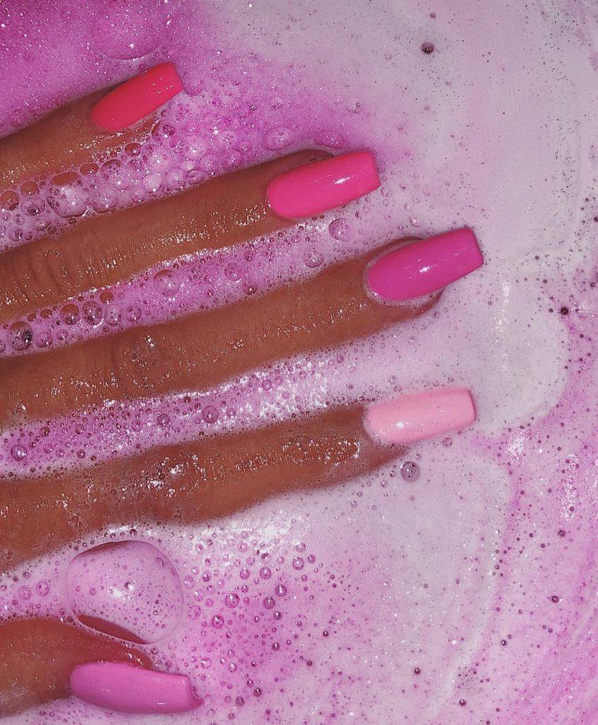Mão branca aberta sobre a água com unha quadrada degradê rosa
