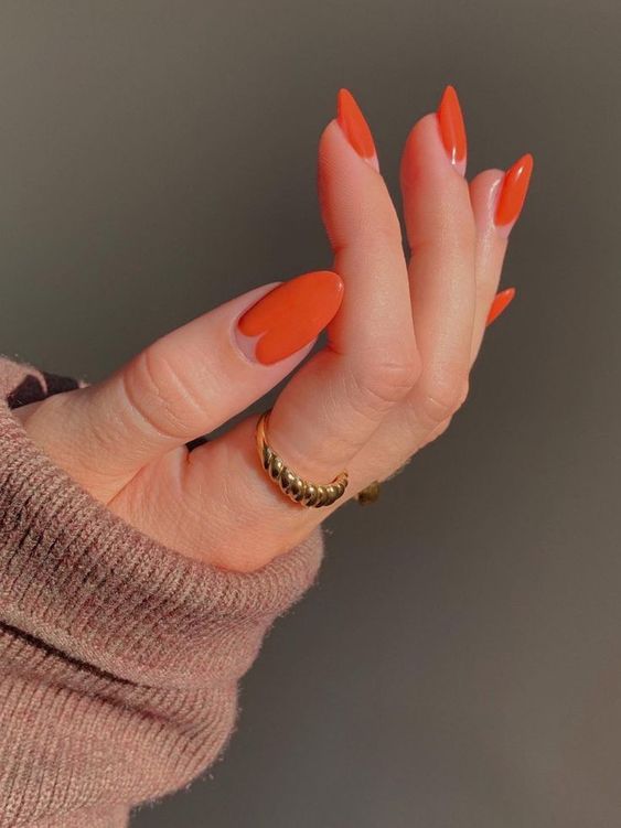 Mão branca com anel dourado e unha laranja decorada 