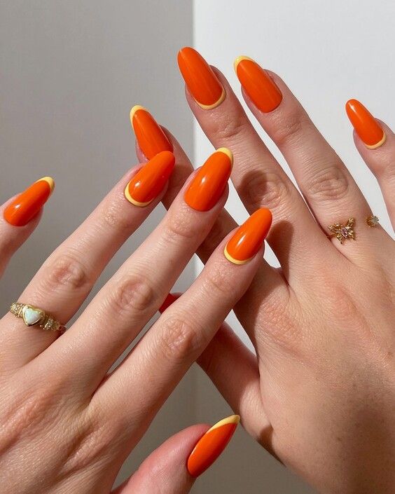 Mãos brancas sobrepostas com unha amendoada laranja com francesinha amarela 