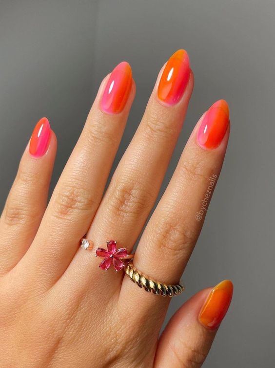 Mão branca com anéis e unha laranja e rosa 