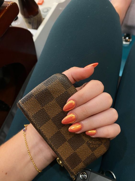 Mão branca segurando uma carteira com unha laranja cromada