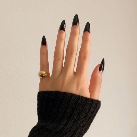 Mão branca com anel dourado e unha preta com design meia lua 
