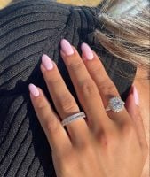 Mão branca com anéis apoiada no ombro com unha amendoada rosinha