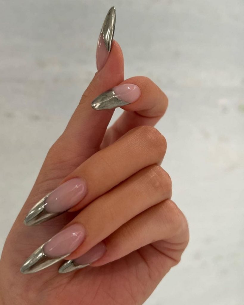 Mão branca com meio fechada com a unha stiletto com francesinha prata metálica