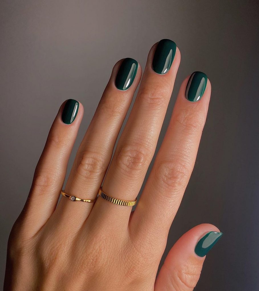 Mão branca com anéis dourados e unha redonda verde escuro