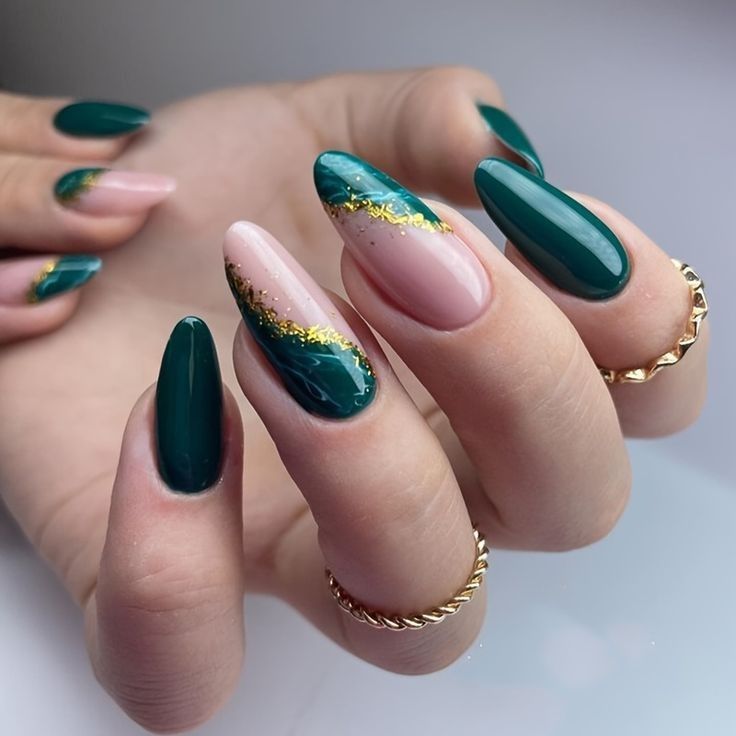Mão branca curvada com anéis dourados e unha verde esmeralda com dourado 