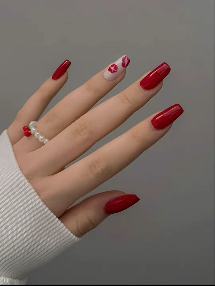 Mão branca com anel de pérolas e unha quadrada vermelha com uma branca com beijos