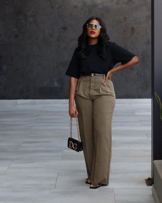 Mulher midsize de pele escura. Elas usa blusa preta e calça verde com cinto.