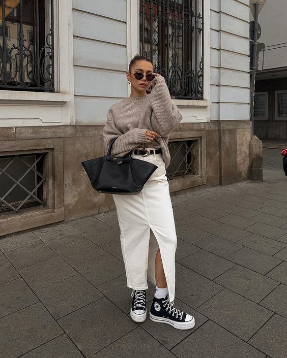 Mulher jovem e magra. Ela usa tricot e saia jeans com cinto