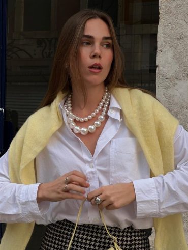 Alesia usando tricô amarelo manteiga, camisa branca, pérolas e saia xadrez