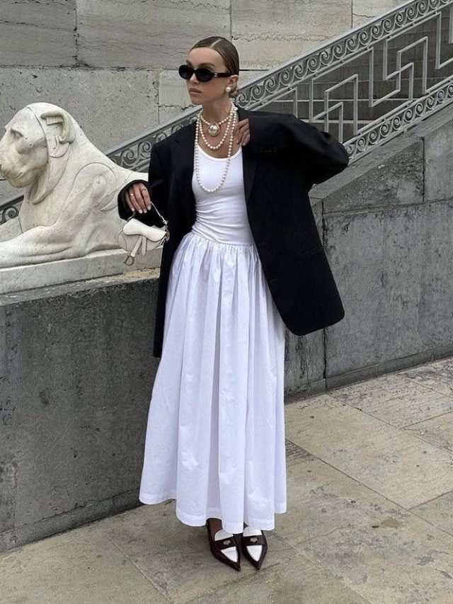 Mulher branca usando blazer, regata branca e saia midi balonê