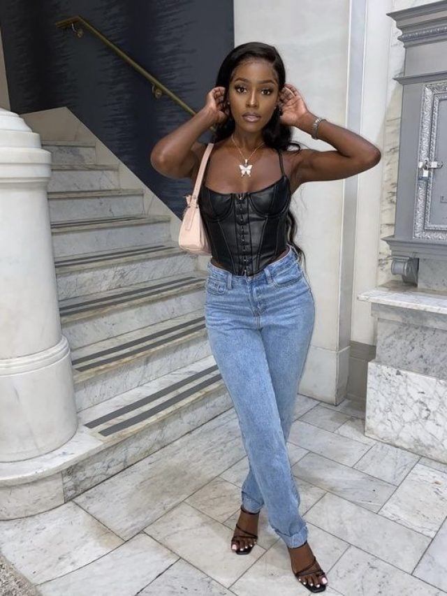 Moça jovem de pele escura. Ela usa corset preto e calça jeans