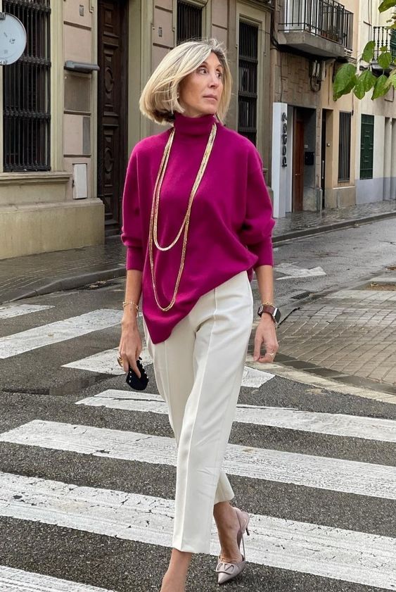 Mulher de 50 anos alta e magra. Ela usa suéter rosa e calça branca com salto alto