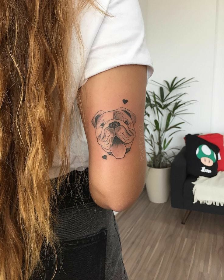 Tatuagem de bull dog com corações atrás do braço e em pele clara