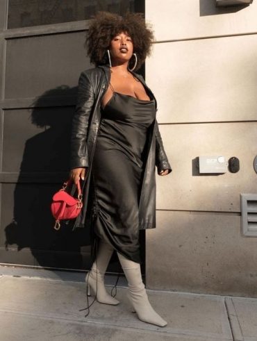Moça jovem de pele escura, ela está de vestido de cetim preto e botas brancas