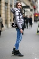 Mulher usando jaqueta metalizada, com bolsa no ombro, calça jeans e coturno.