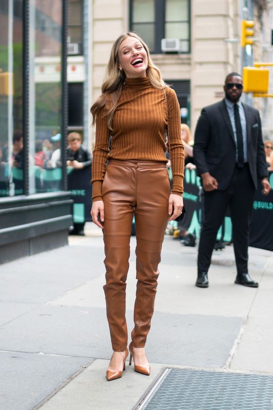 Mulher jovem e loira, usando blusa marrom e calça de couro marrom.