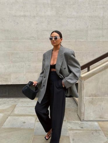 Mulher com cabelo preso em coque, usando blazer oversized cinza e calça de alfaiataria preta.