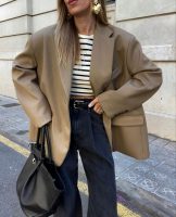 Mulher branca usando blazer oversized, brinco maximalista em formato de coração, blusa listrada, calça jeans e maxi bag preta