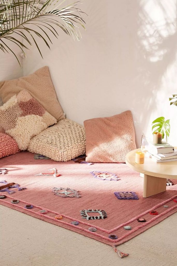 Espaço com tapete rosa e almofadas