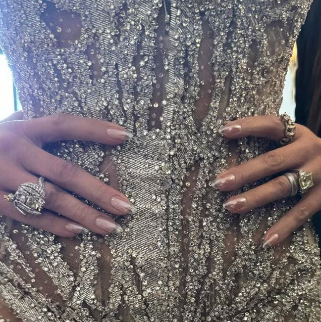 Jennifer Lopez com as mãos cheias de anéis na cintura e com a unha cintilante transparente 
