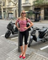Linda usando blusa ombro a ombro xadrez rosa, bolsa preta, óculos de sol minimalista, calça capri e sapatilha vermelha envernizada