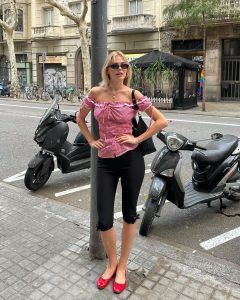 Linda usando blusa ombro a ombro xadrez rosa, bolsa preta, óculos de sol minimalista, calça capri e sapatilha vermelha envernizada