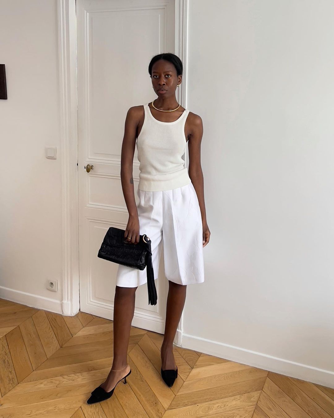 Sylvie Mus usando regata branca, jorts de alfaiataria branco, bolsa preta e mule preto