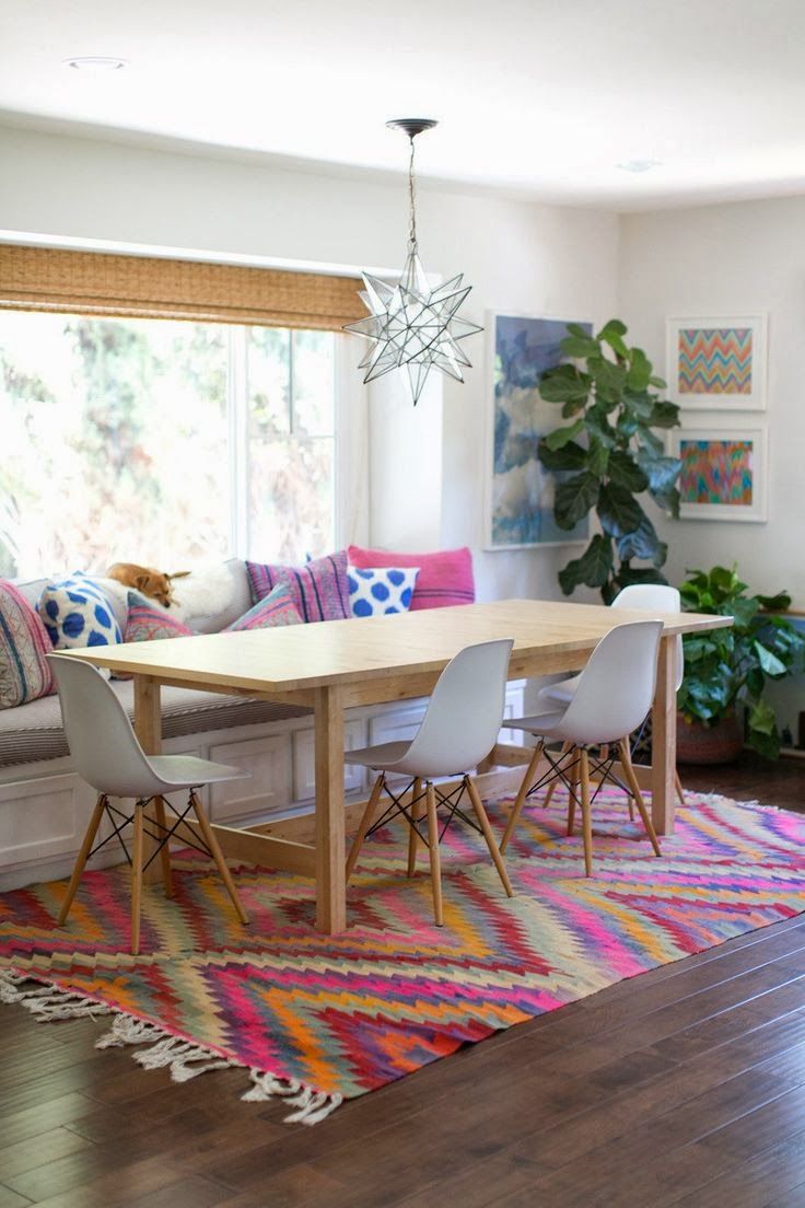 Sala de jantar com mesa em madeira, cadeiras brancas e tapete colorido