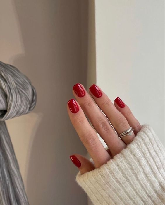 Mão branca com anel e unha curta quadrada vermelha 