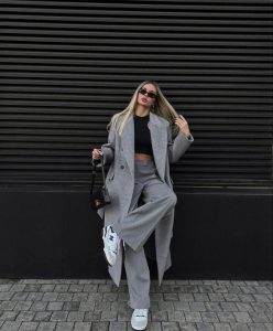 Mulher vestindo look com sobretudo cinza e calça de alfaiataria cinza.