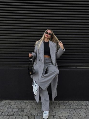 Mulher vestindo look com sobretudo cinza e calça de alfaiataria cinza.
