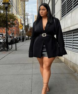 Mulher plus size, com cabelo moreno, usando saia de couro em preto, blazer preto com cinto.