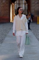 Mulher jovem, magra e de pele clara. Ela está vestindo um look todo branco com colete de tricot.