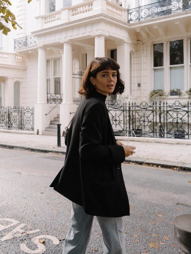 Chloe Miles com corte de cabelo french bob, usando jeans e blazer preto