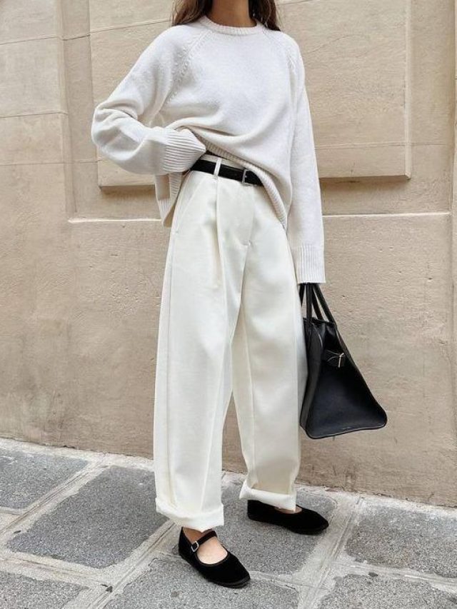 Mulher jovem branca usando tricô branco, calça de alfaiataria branca, maxi bag preta e sapatilha preta de veludo