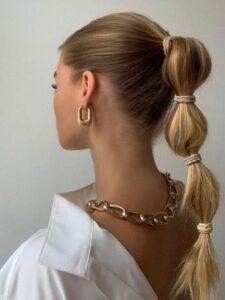 Mulher branca e loira, com cabelo longo preso em penteado bubble braids