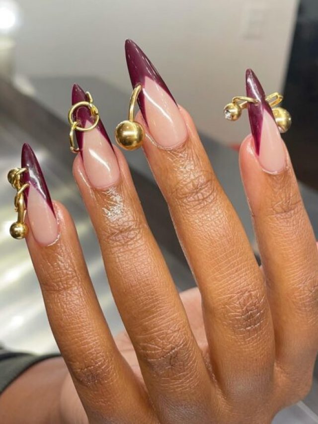 Mão negra com unha stiletto francesinha vermelho cereja e com piercings dourados
