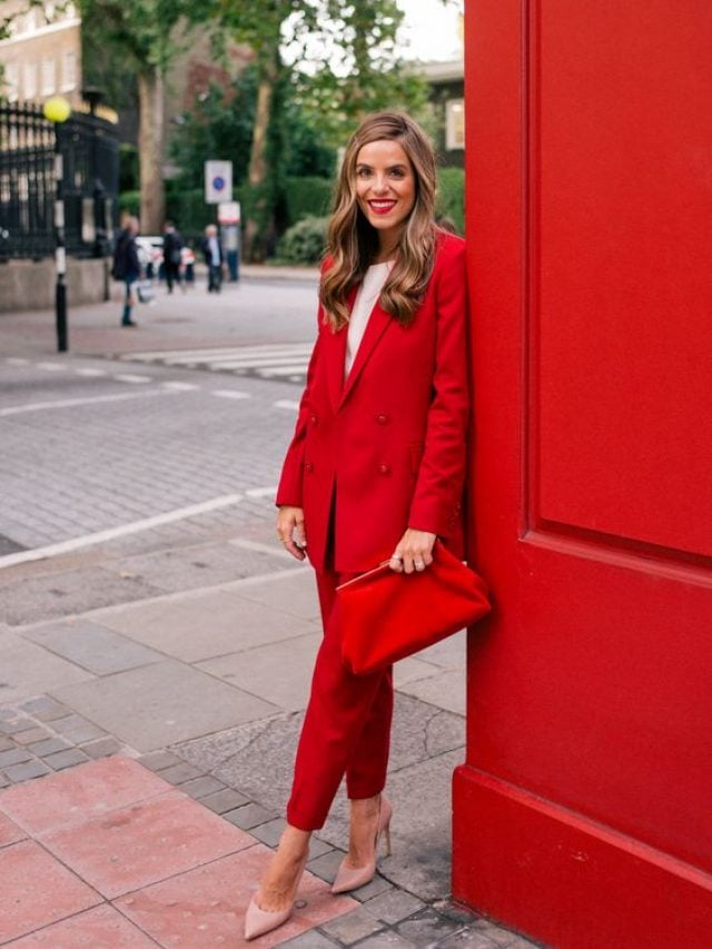 Mulher com cabelo curto e loiro, usando look monocromático em vermelho, segurando bolsa vermelha e usando blazer vermelho.