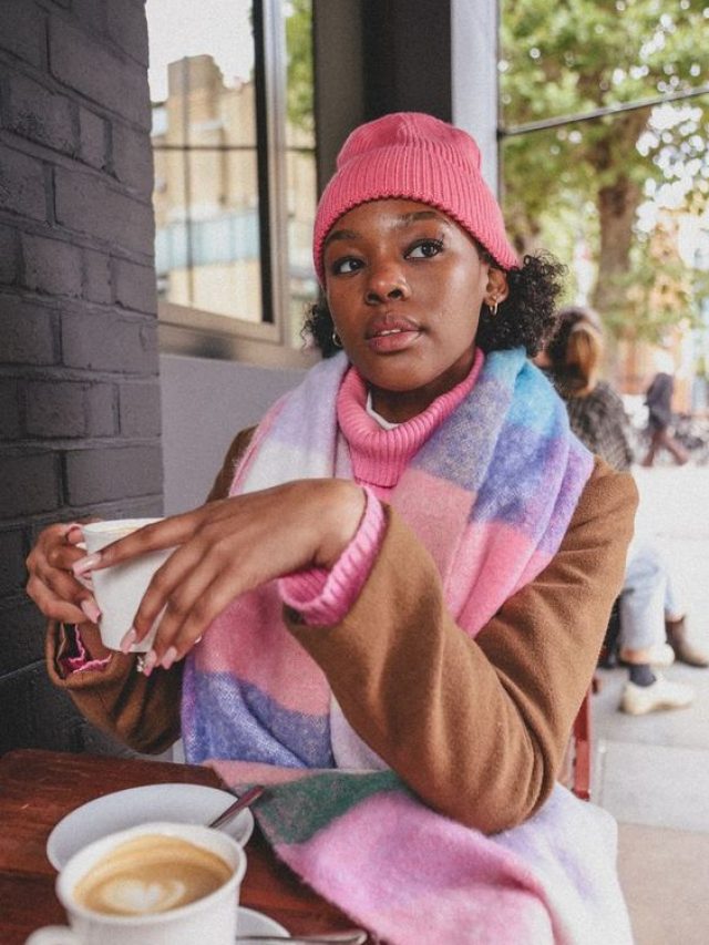 Mulher jovem de pele negra. Ela usa touca rosa e cachecol colorido.