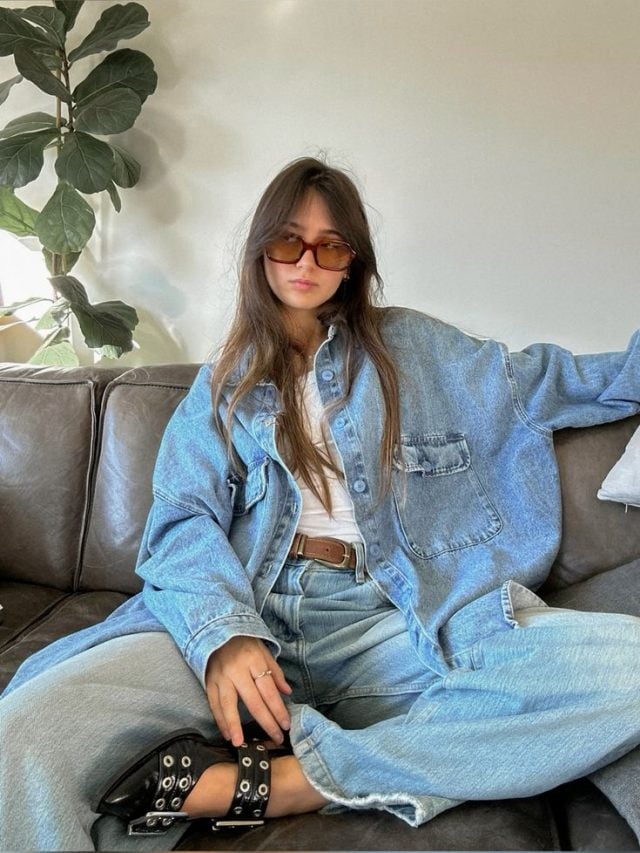 Mulher jovem de pele clara. Ela usa jaqueta jeans, camiseta branca e calça jeans.