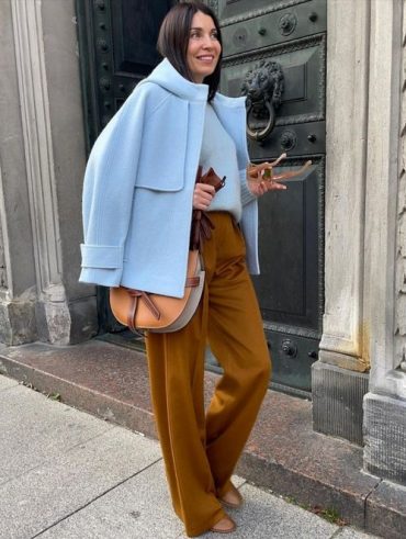 Mulher jovem e com cabelo moreno, usando casaco de lã batida em azul claro e calça em cor amarelo queimado.