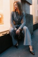 Mulher jovem e loira, sentada e usando look monocromático com calça de alfaiataria cinza e braceletes dourados.