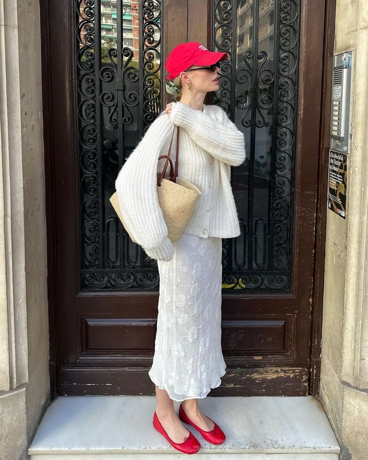 Linda usando boné vermelho, cardigan off-white, bolsa de palha, saia midi texturizada branca e sapatilha vermelha