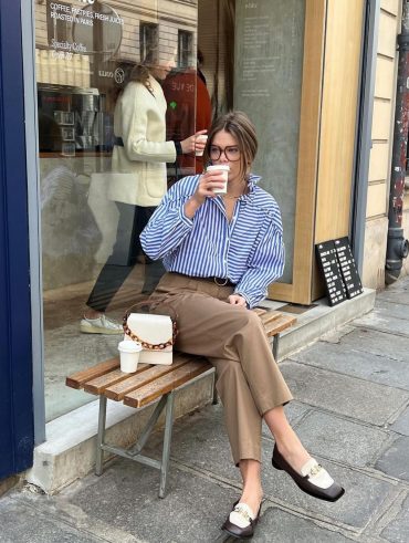 Elodie Romy usando camisa listrada azul, calça de alfaiataria reta, bolsa off-white e loafer bicolor