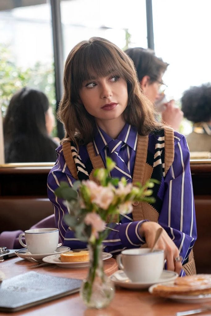 Emily de Emily em Paris usando colete marrom Miu Miu com uma camisa listrada Sébline primavera 2024 e gravata para um visual chique de escritório